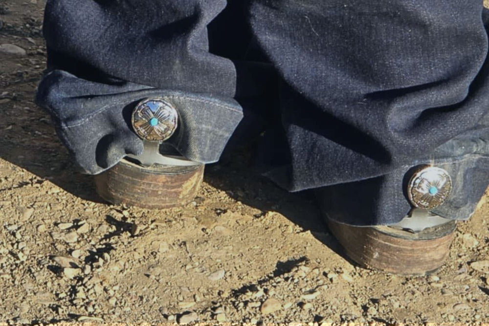 Close-up of bootcut jeans and cowboy boots fitted with Cowgirl Cuff western accessories designed to prevent dragging jean hems and protect denim from wear.
