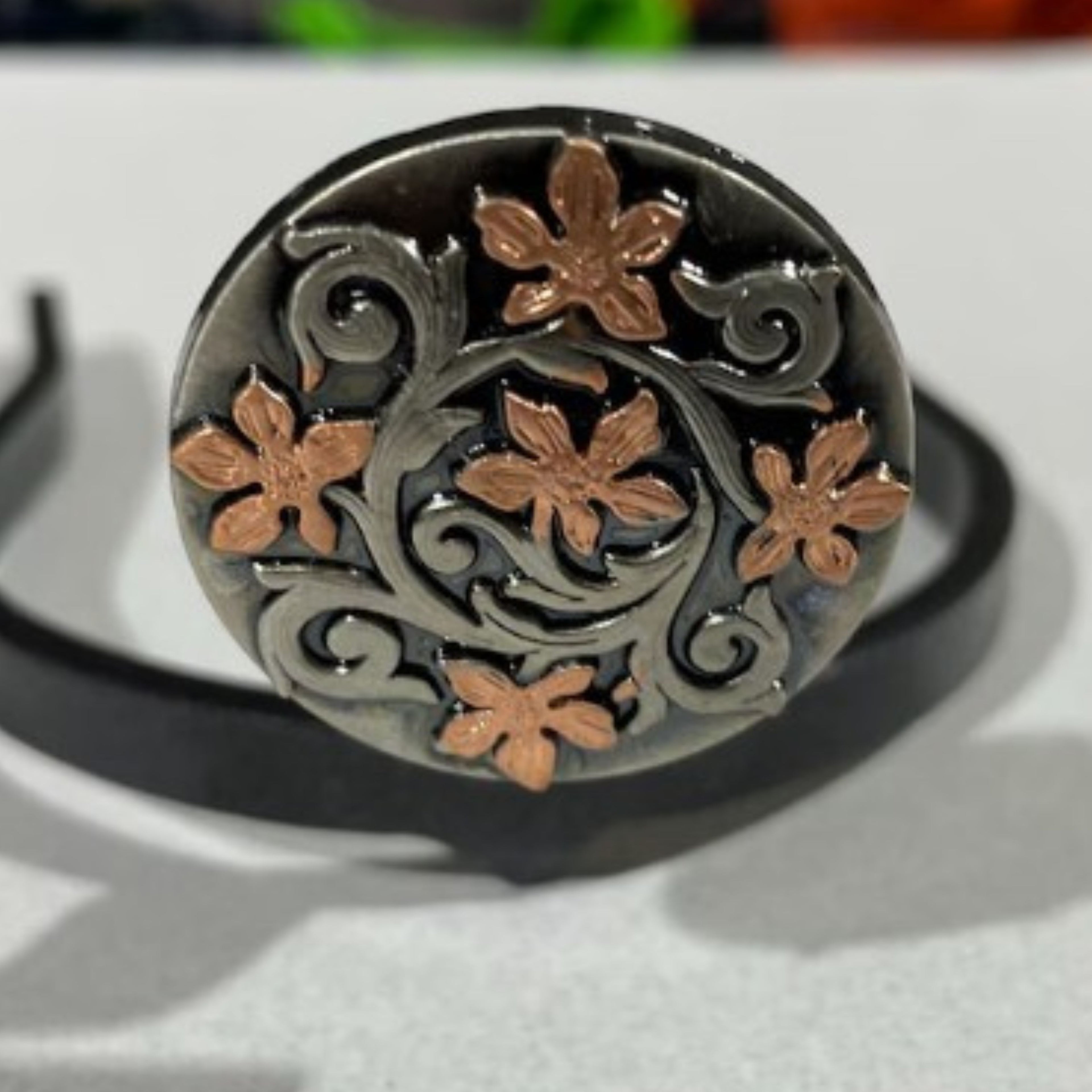 Close-up of the Floral Cowgirl Cuff showcasing copper-tone floral accents and flowing western vine scrollwork on a dark metal background.